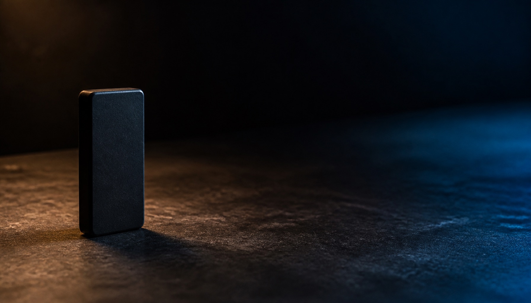 A single domino standing upright and alone at the near end of a long empty dark surface