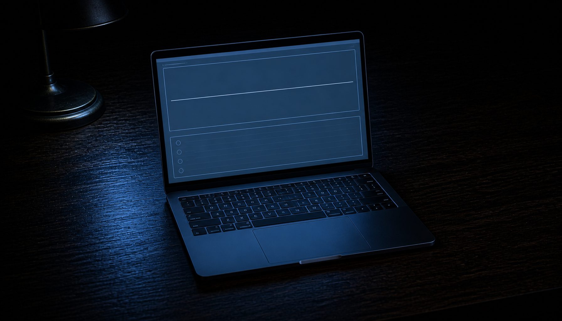 An open laptop in a dark room showing an empty monitoring view, its screen the only light source, the desk lamp switched off